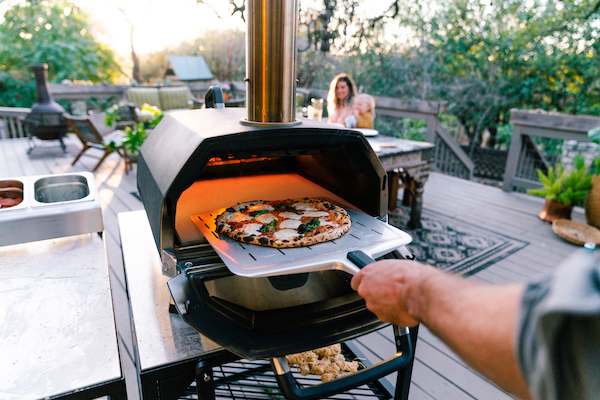 Ooni Karu 16 pizza oven multi fuel met een heerlijk gebakken pizza op pizzaplank die net uit de oven komt.